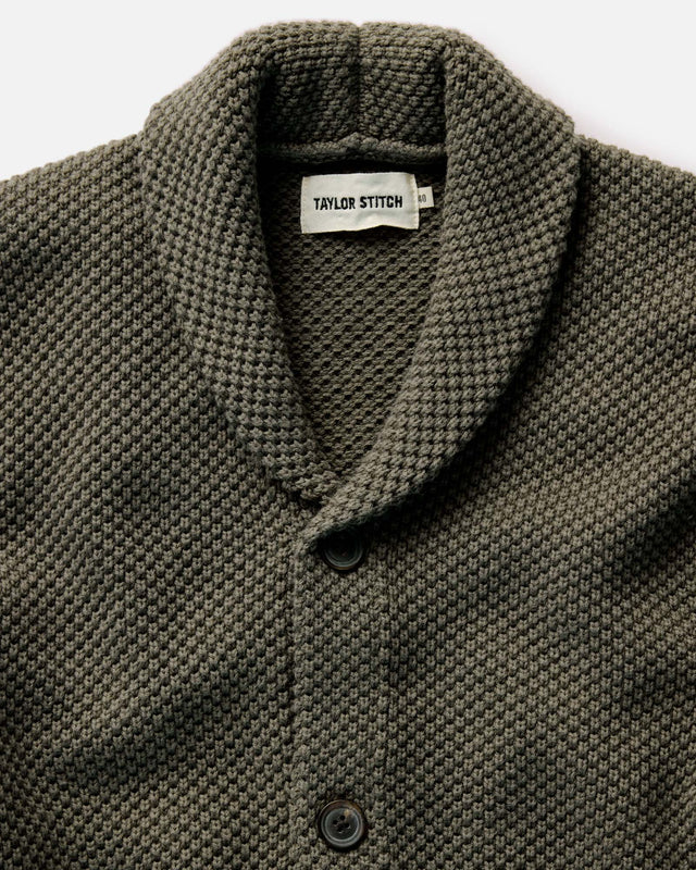 Close-up of a green knit shirt with 'Taylor Stitch' label on a white background
